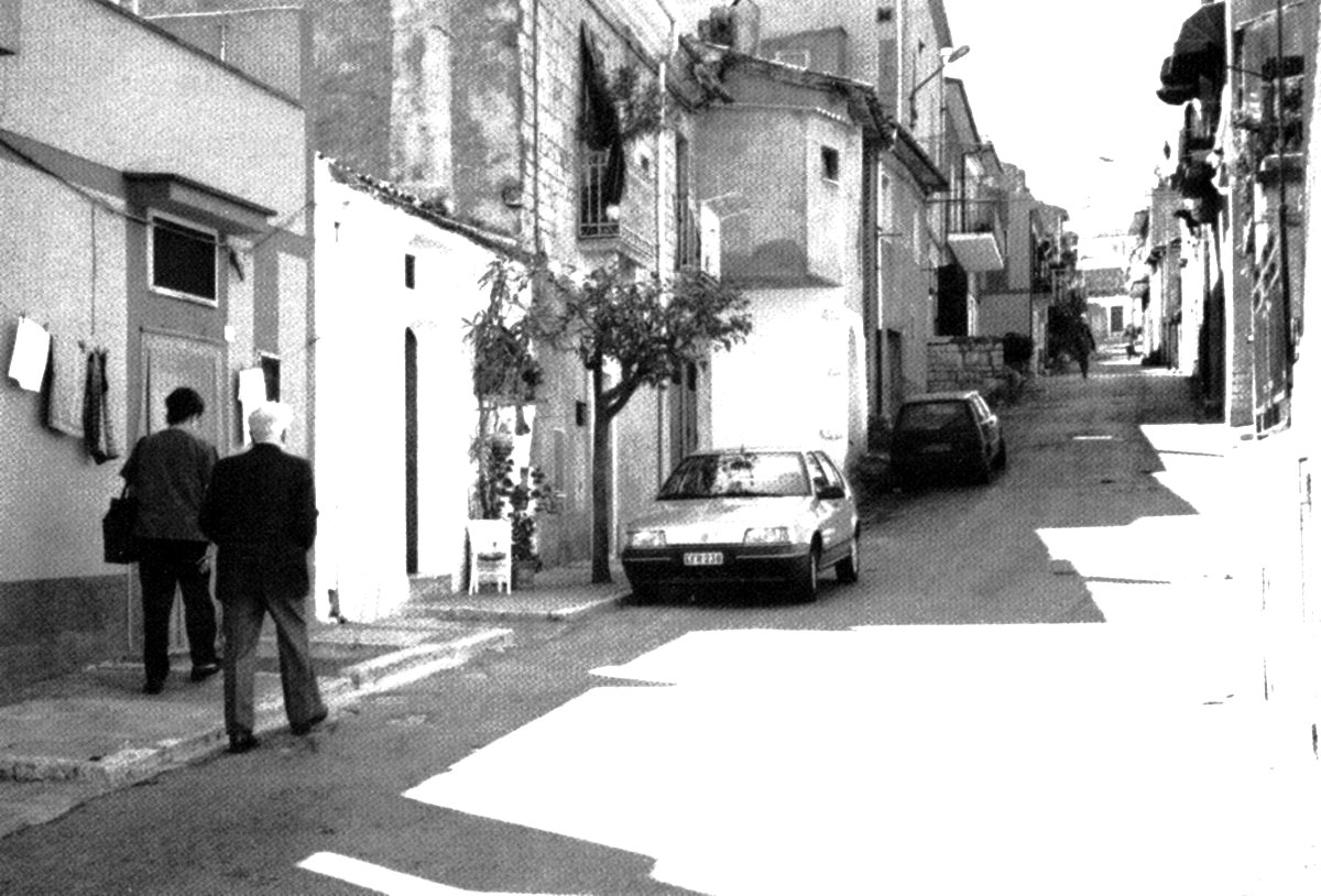 Two men walking along a narrow street of whitewashed houses in Maschito